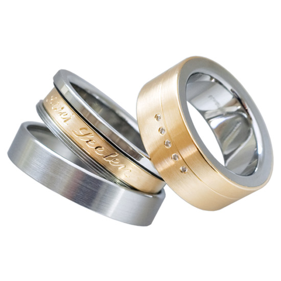 Editing:
Forged, turned, engraved, hallmarked, polished
Surface texture:
Matt, polished inside
Materials:
Stainless steel, yellow gold, diamonds
Above all, special feature:
These elegant rings have an individual engraving on the inside band in gold or platinum. Like a medallion, the personal message of these unusual partner rings is carried inside the safe rings.
Shape:
Ring with square profile
Category:
Friendship ring, wedding ring, wedding ring, partner ring, proposal ring, jewelry ring, poetry ring, message ring
Style:
modern design
Ring width:
8mm
Material thickness:
2.3mm
Stone setting:
Rubbed diamonds
Elegant designer wedding rings, partner rings, proposal rings or jewelry rings with an individual engraving that is worn hidden inside the opening rings. The 8mm wide smaller ring has a core made of durable stainless steel covered with a 0.5mm thick layer of matt 18 carat yellow gold. The engraved band is also made of yellow gold. There are 5 brilliant-cut diamonds of 0.025 carats of very good quality set in a line. The larger ring is made of stainless steel, the inner band is made of 18 carat yellow gold. The rings are comfortable to wear thanks to the profile and the broken edges. The rings are sustainably produced and 100% made in Germany. The diamonds come from conflict-free sources.